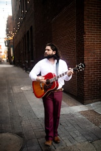 a man holding an acoustic guitar on a street